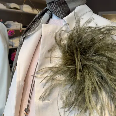 Helle Jacke mit einem grauen Tuch und einem grünen Federbüschel als Accessoire in der Brusttasche