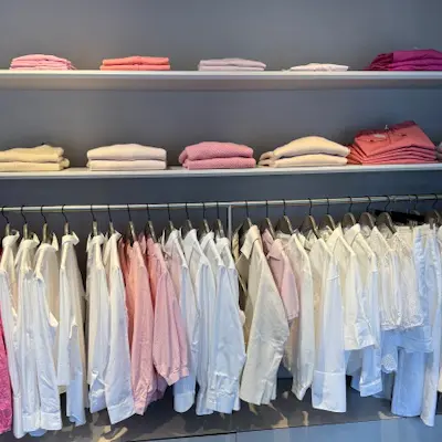 Blusen in weiß und Rosa-Tönen sowie Pullover in passenden Farben hängend bzw. liegend in einem Regal